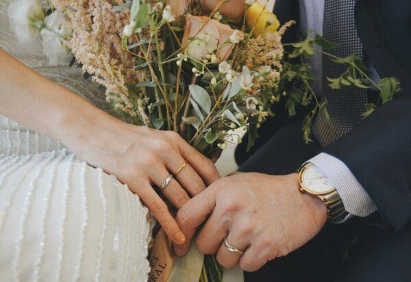 Groom and Bride's hands wearing wedding rings with a bouquet