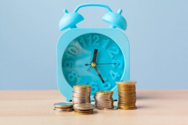 Stack of money coins in front of a blue alarm clock