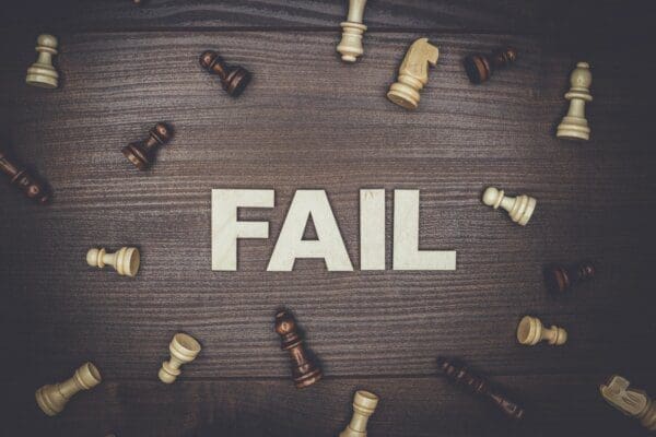 fail spelled with white letters surrounded by chess pieces on a wooden background
