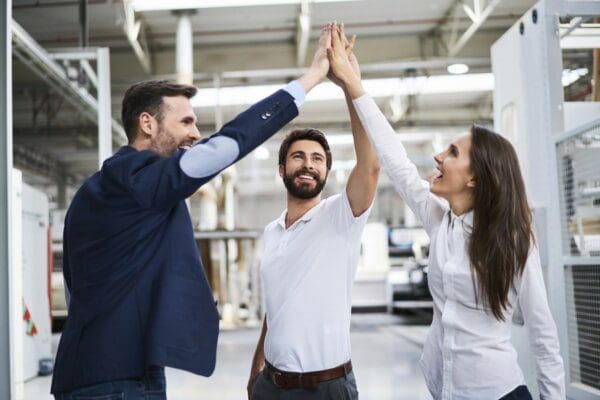Happy businessman and employees high-fiving in a factory