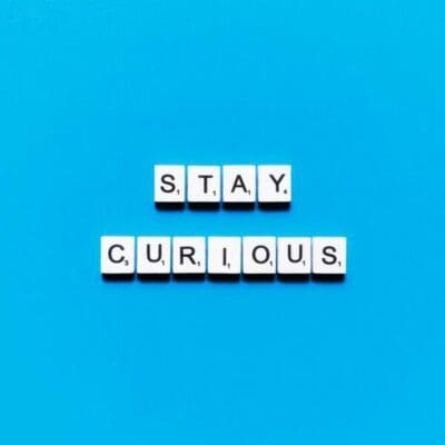 Stay curious written in scrabble tiles on a blue background