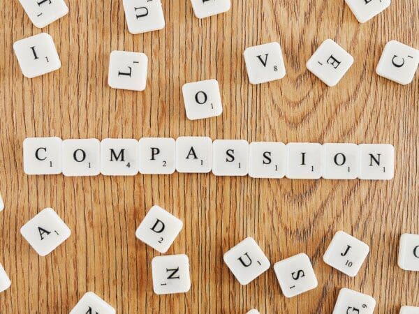 “Compassion” written with scrabble tiles on a wooden surface