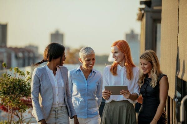 Four female colleagues in a dynamic team looking at an iPad outside