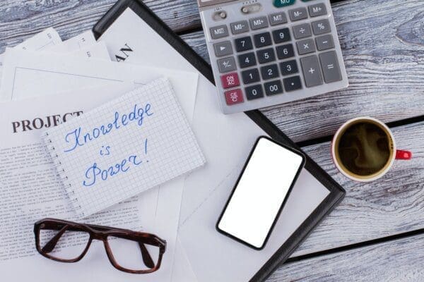 Knowledge is power written on notepad with calculator, glasses, and phone next to it