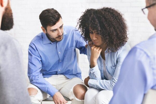 Supportive people comforting sad woman at group therapy meeting