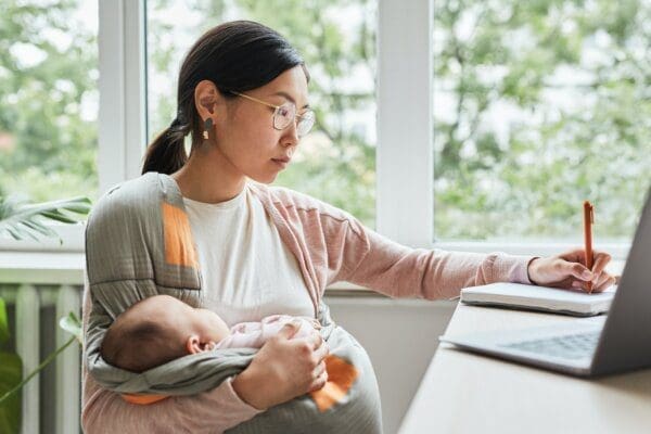 Working mother on notepad at desk with baby in her arms