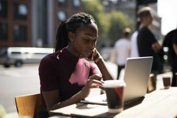 African American woman working remotely on her laptop from a cafe outside