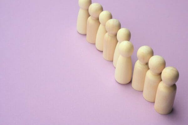 Wooden men figures in a row with leader figure out of line