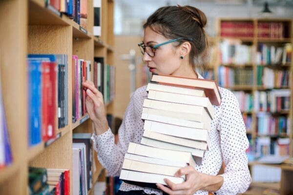 Young woman with a stack of books in library looking to learn more