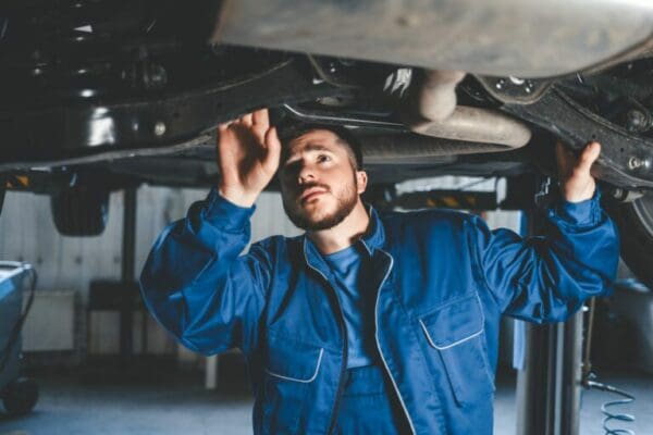 Auto mechanic wearing blue while inspecting underneath a car and Diagnostics of the condition of the car