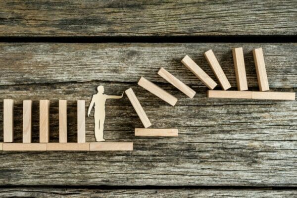 Wooden man stopping a domino effect on two wooden shelves