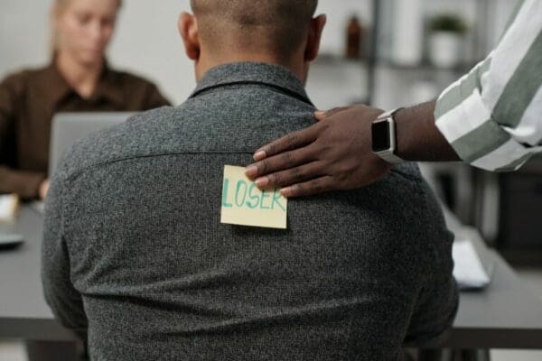 Hand of a man putting a loser note on back of colleague shows bullying and unethical behaviour