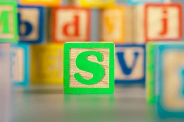 Green letter S toy block with blurred alphabet blocks in the background