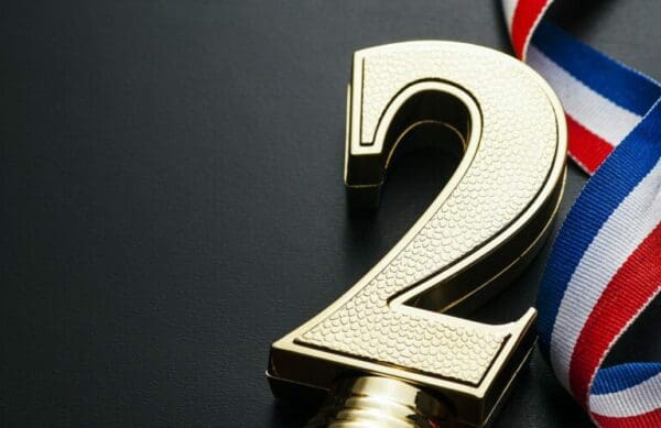 Gold number two next to blue, red and white award ribbon on grey surface