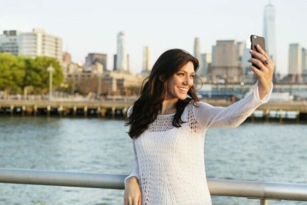 Happy self-centred ESTP Woman Taking Selfie While Standing On Promenade With One World Trade Center In Background