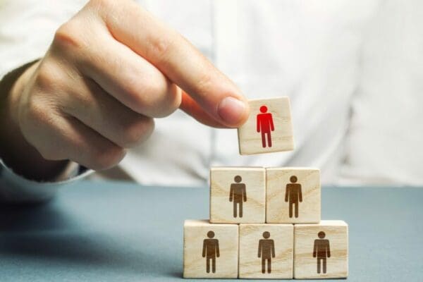 Hand of manager putting Laissez-Faire leader block on top of organisation heirarchy