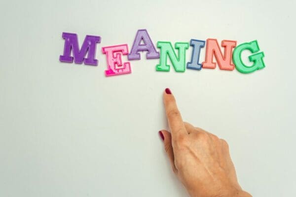 meaning word spelt with colourful letter magnets with red nail painted index finger of female hand pointing to it