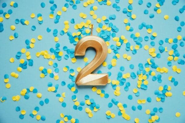 Number 2 two golden celebration birthday candle on yellow and blue confetti Background