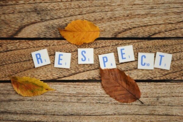 Respect spelled with white word scramble tiles next to autumn leaves on a wooden table