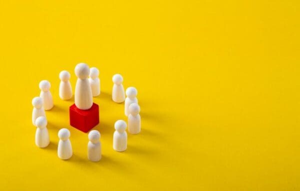 Strategic leader wooden figure on a red podium surrounded by followers on yellow background