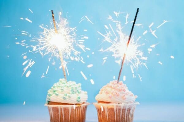 Similar blue and pink decorated cupcakes with sparklers against a blue background