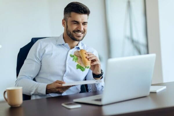 Happy businessman eating sandwich and using laptop on a break in the office