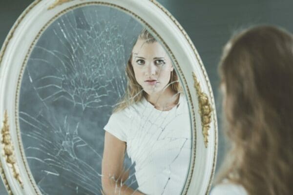 Teenage girl with narcissistic personality disorder problems looking in a shattered mirror