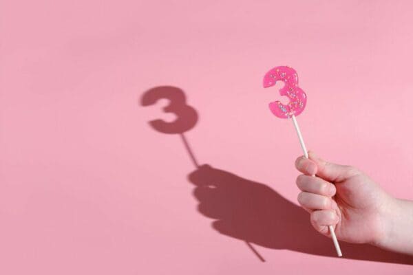 girl's hand holding a number 3 shaped lolipop