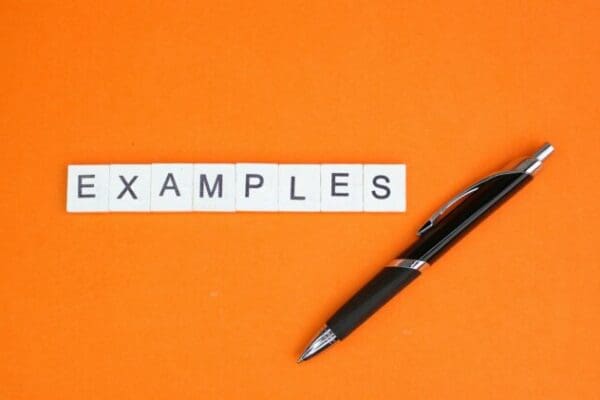 Examples spelled with white cubes on orange surface next to black pen