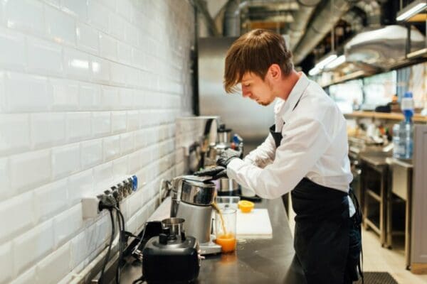Male waiter preparing beverage in kitchen after asking 'is everything okay?'