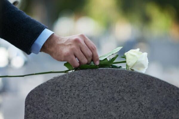 Hand of a man placing a white rose on his dad's grave
