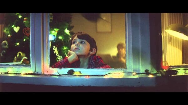 Young boy looking through window with christmas lights