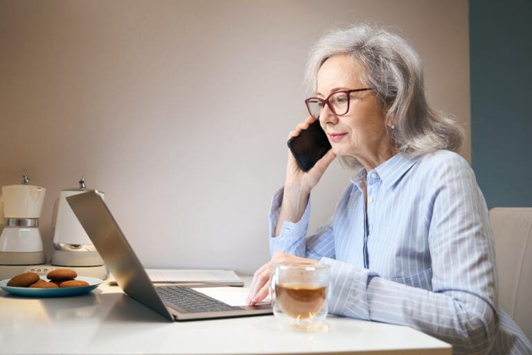 Active elderly lady works from home using a phone and laptop