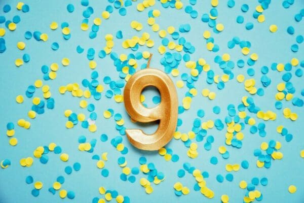 Number 9 nine golden celebration birthday candle on yellow and blue confetti Background