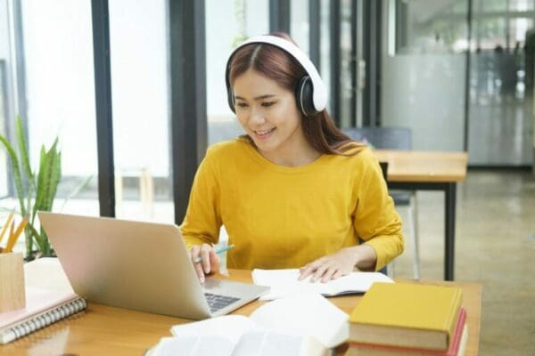 Woman learning virtually online using laptop and writing notes