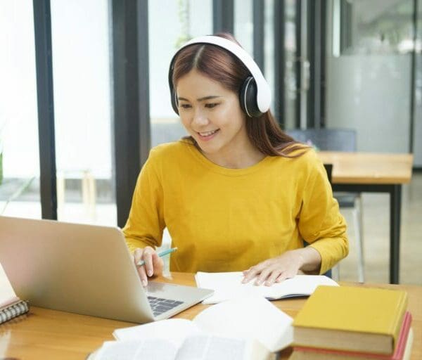 Woman learning virtually online using laptop and writing notes